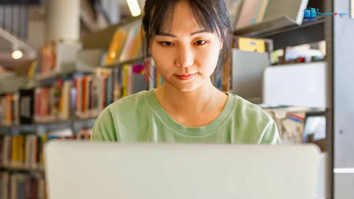Phụ nữ trẻ châu Á tại thư viện đang học và sử dụng máy tính xách tay