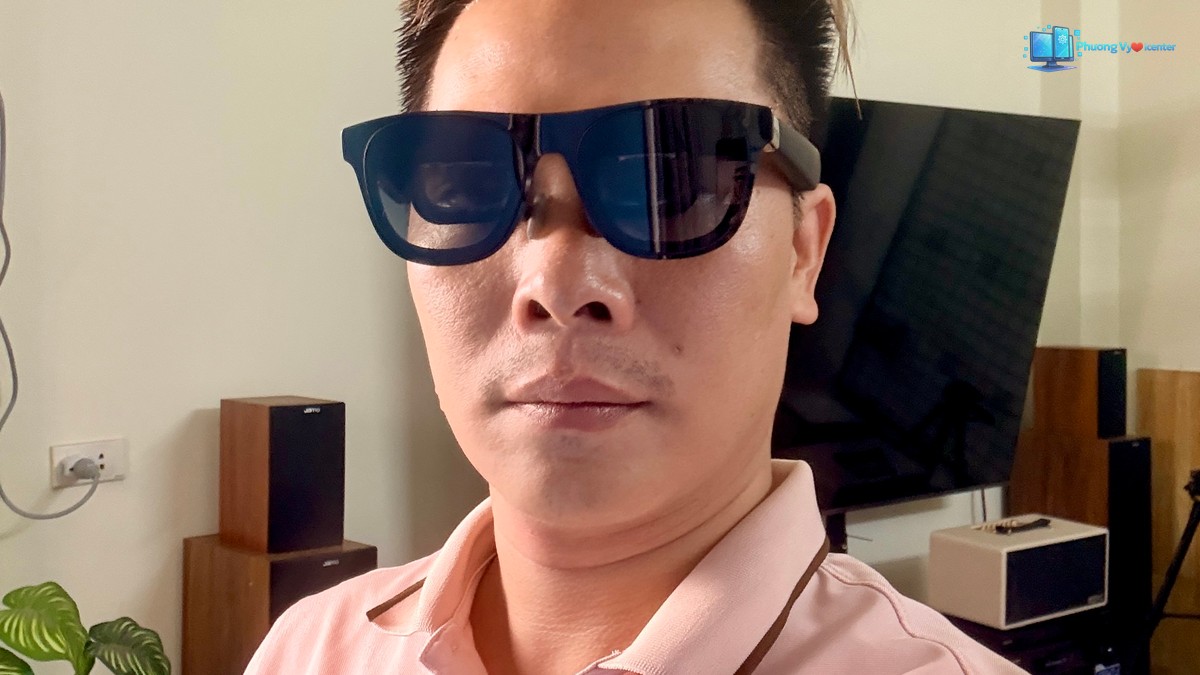 Người mặc áo hồng đeo XREAL One Pro trong phòng có tivi và loa