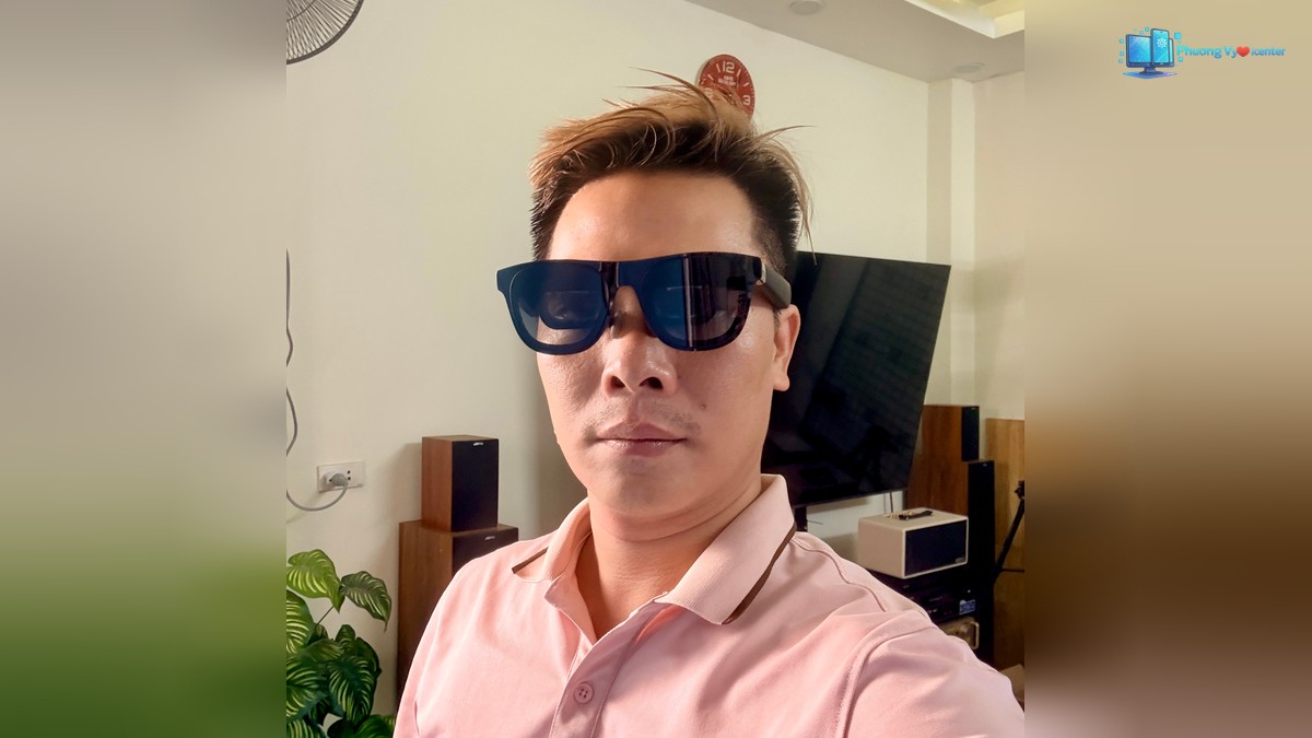 Người mặc áo hồng đeo XREAL One Pro trong phòng có tivi và loa