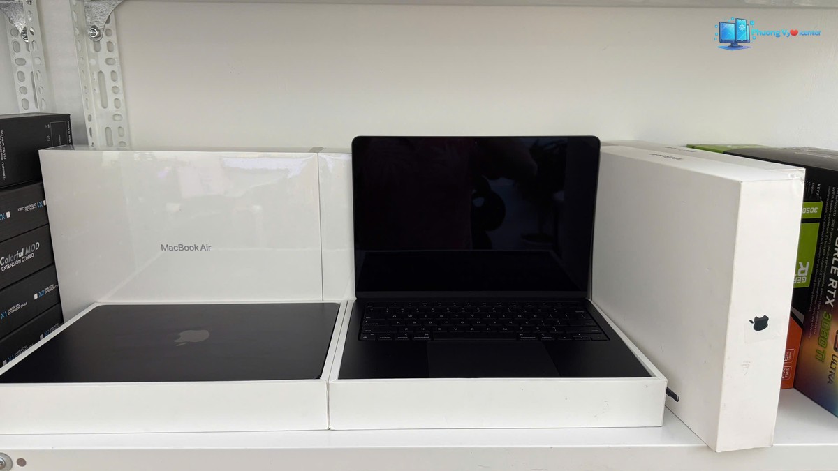 Apple MacBook Air M3 mở với màn hình tắt, đặt giữa các hộp và khay đựng máy
