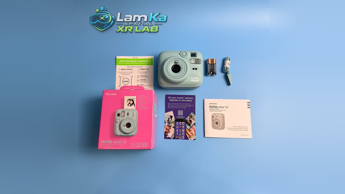 Fujifilm Instax Mini 13 cùng hộp, pin, dây đeo và tài liệu trên nền xanh